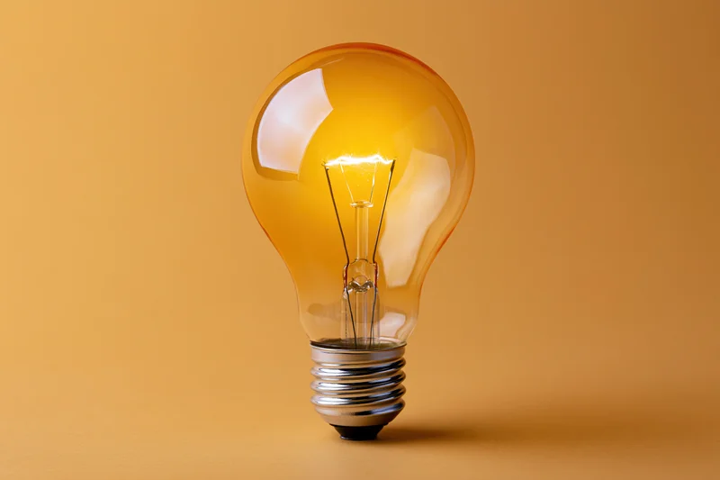 Glowing incandescent light bulb with visible tungsten filament on warm orange background