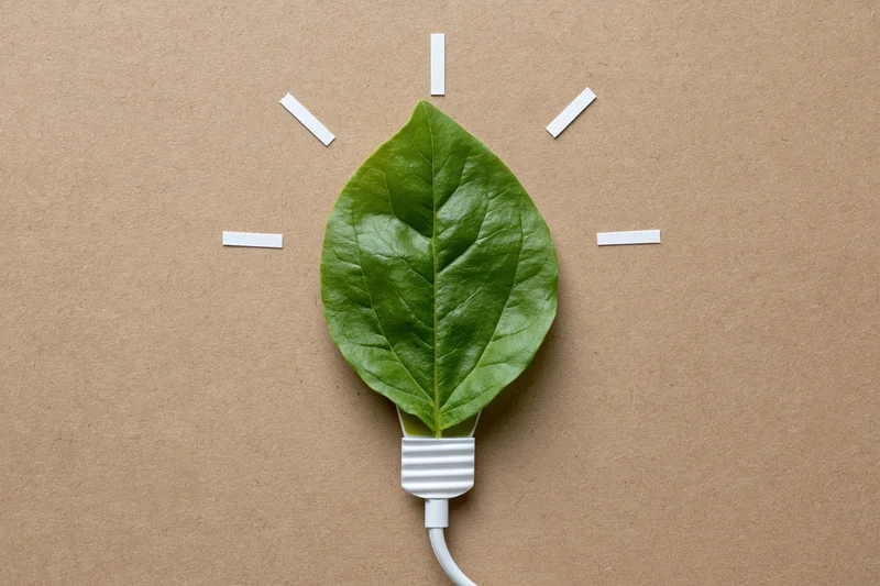 Green leaf shaped like a lightbulb with white cable on kraft paper background