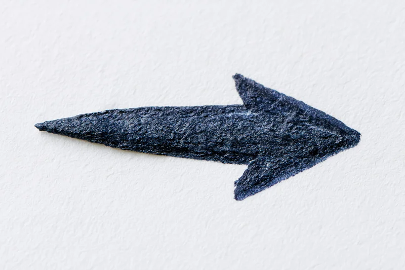 Hand-drawn dark arrow pointing right on white textured paper