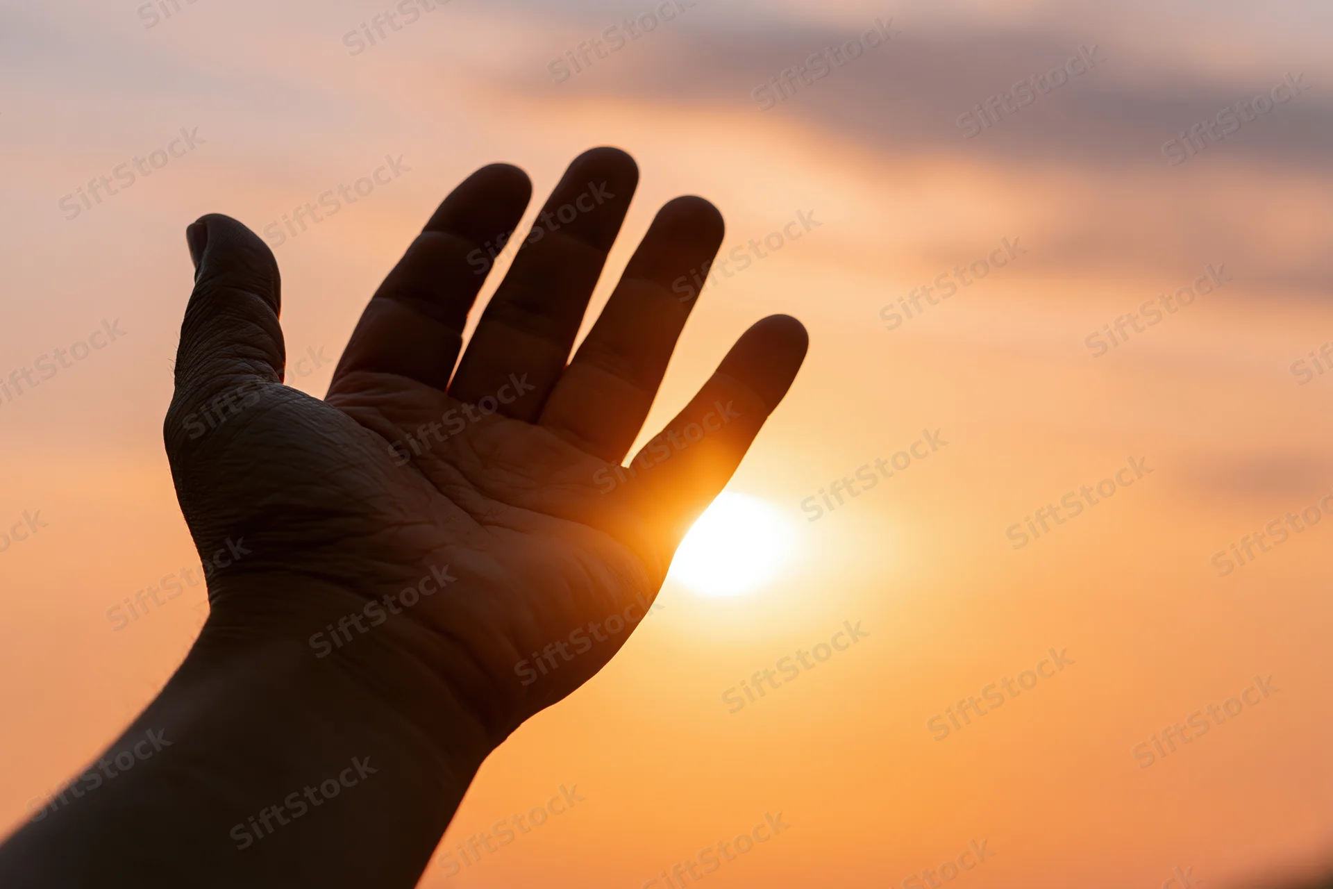 Hand held open palm-up against glowing sunset sky