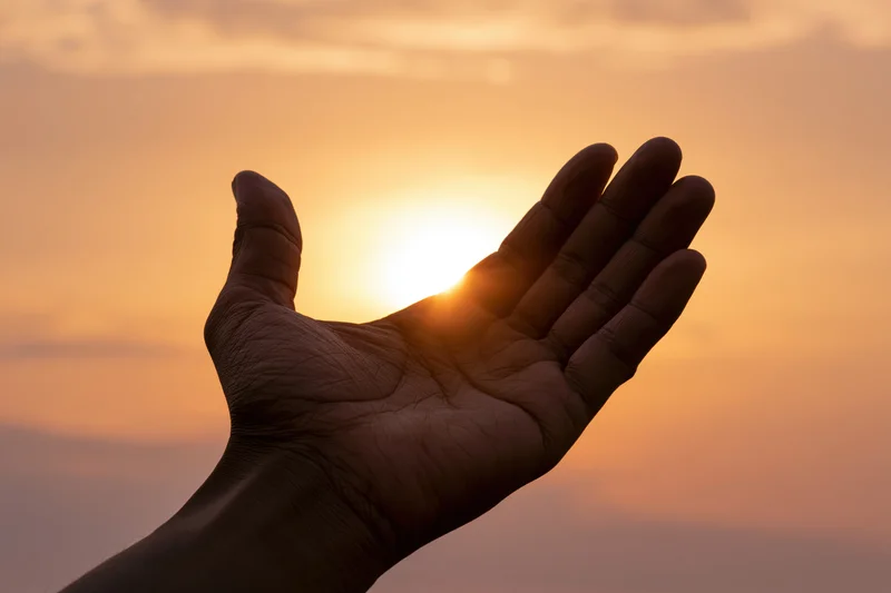 Open hand held palm-up against glowing sunset sky