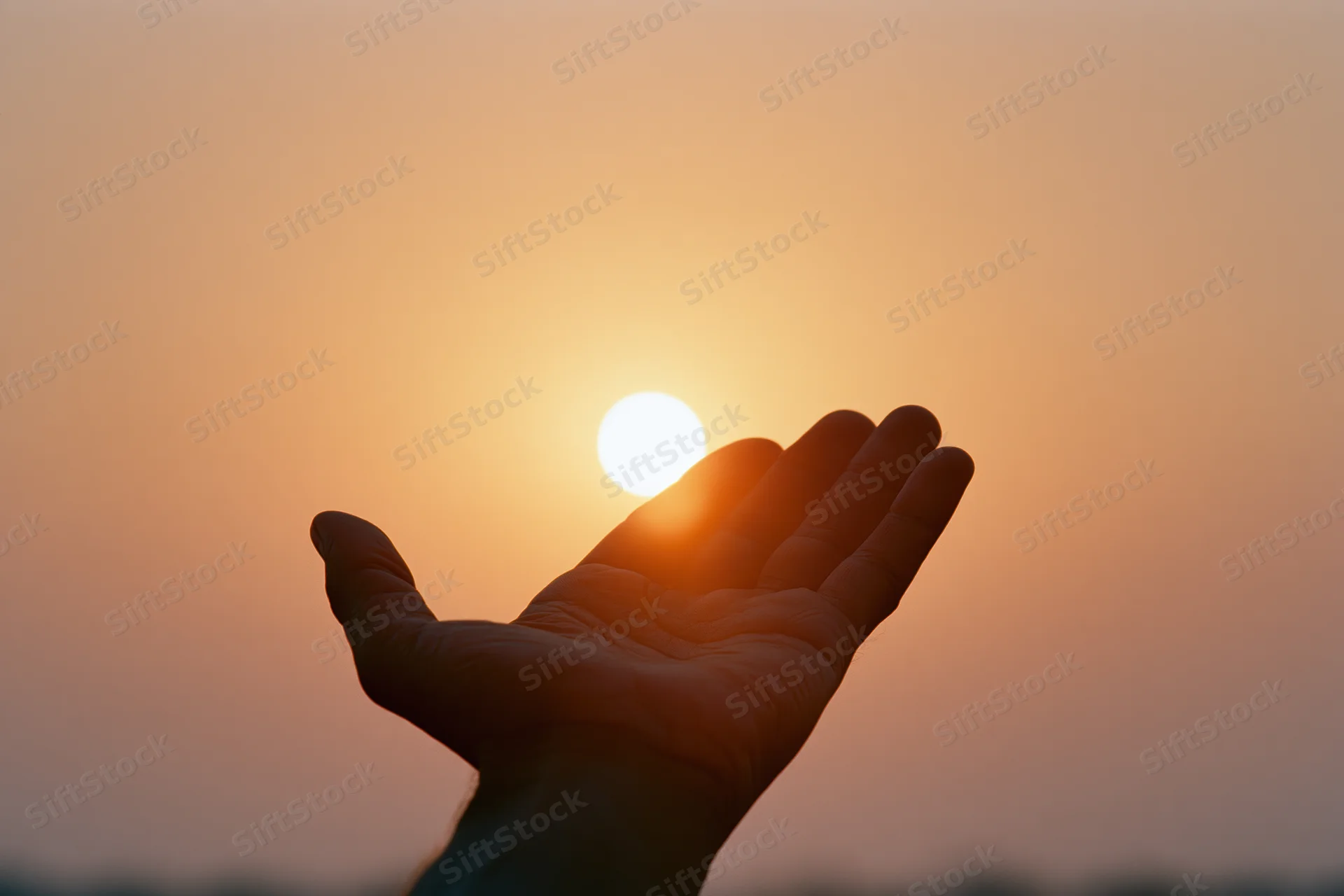 Hand held palm-up against setting sun in warm sky