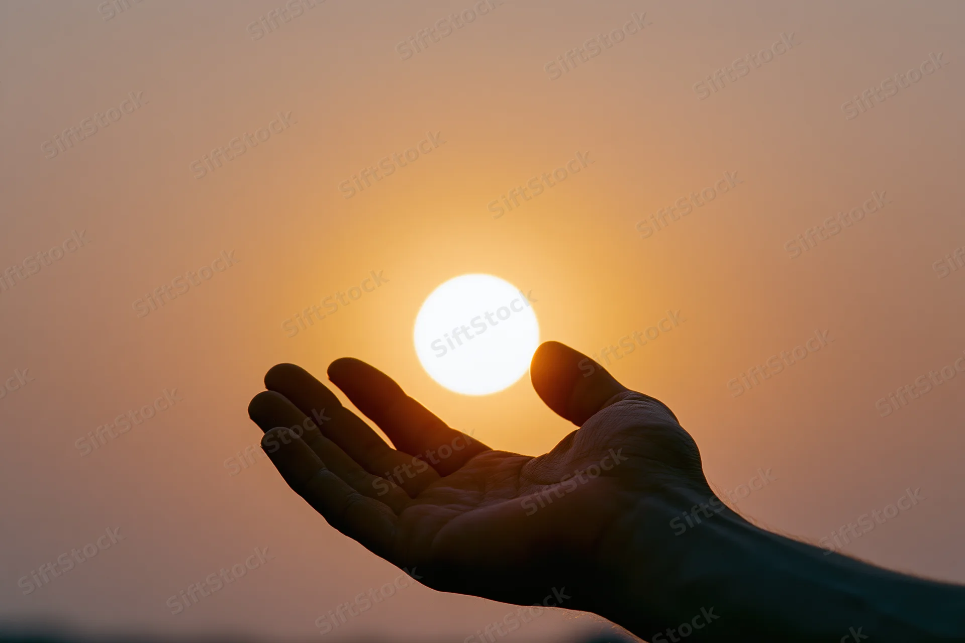 Hand held palm-up against setting sun in warm sky