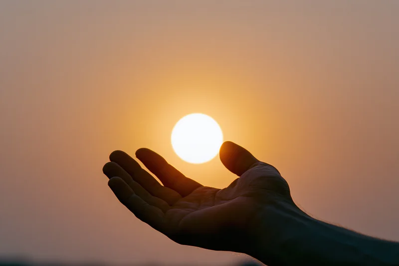 Hand held palm-up against setting sun in warm sky