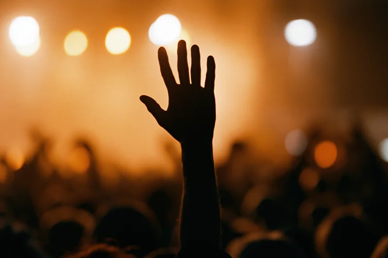 Hand raised above crowd at concert stage with glowing lights
