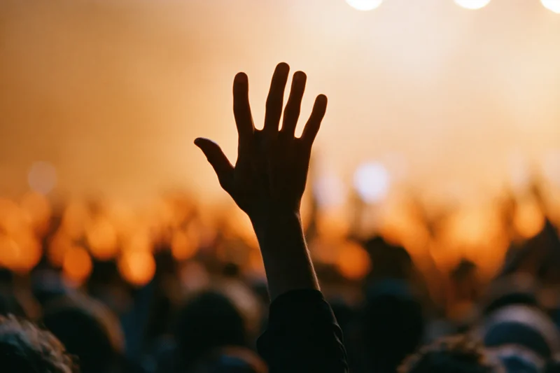 Hand raised above a crowd at a concert under stage lights