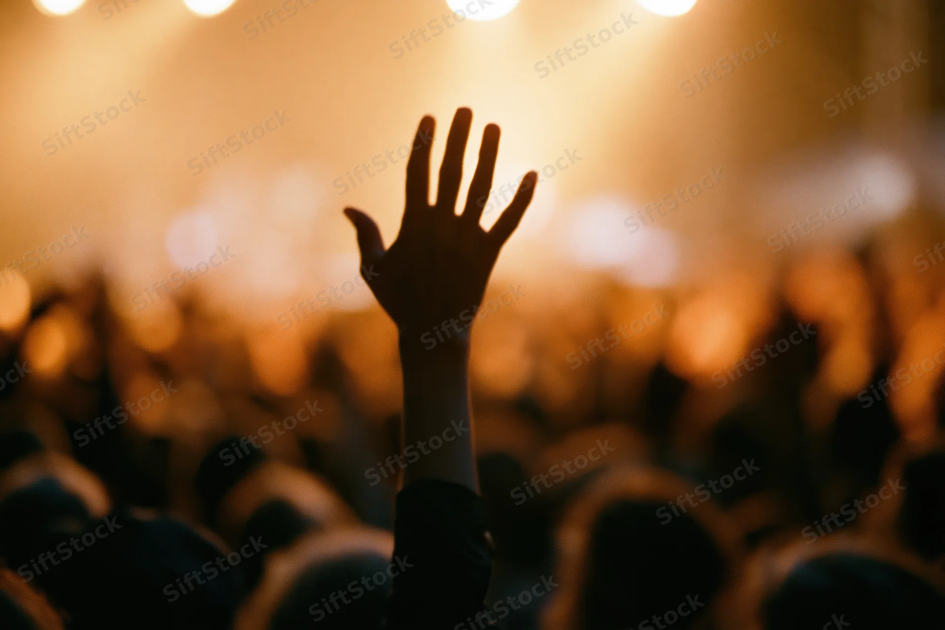 Hand raised above a crowd at a concert under stage lights