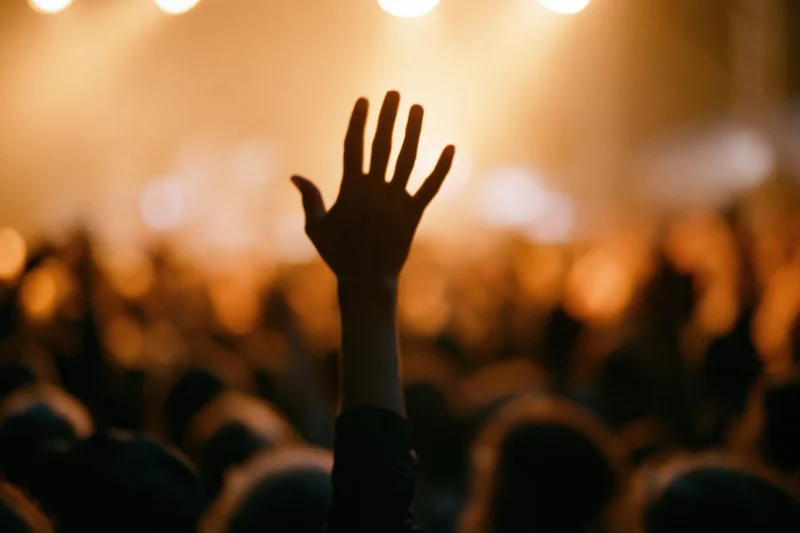 Hand raised above a crowd at a concert under stage lights