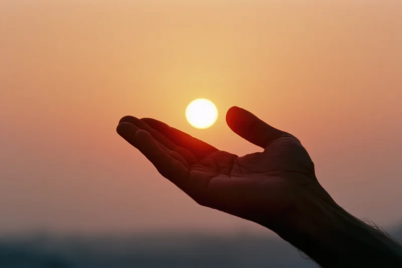 Open hand silhouetted against a glowing sunset sky