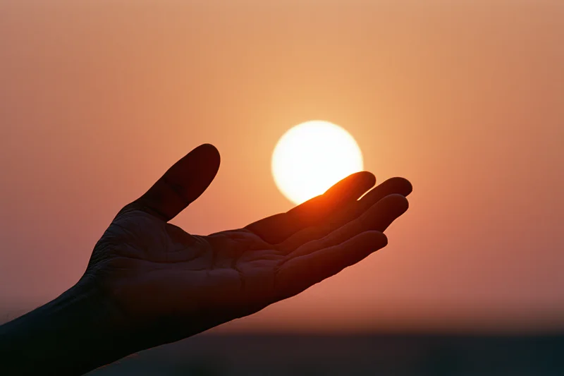 Hand held palm-up in silhouette against a setting sun at dusk