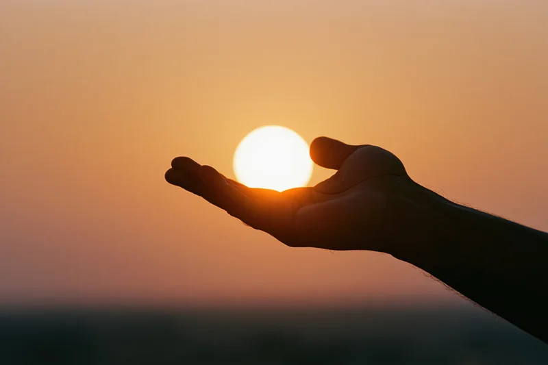 Hand held palm-up in silhouette against a setting sun at dusk