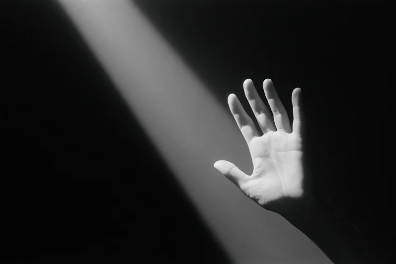Hand reaching upward into a diagonal beam of light against a dark background