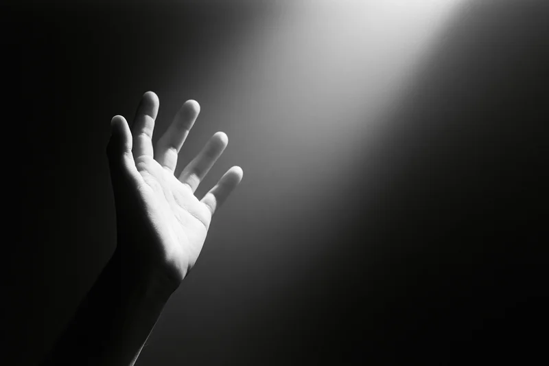 Hand reaching upward into a spotlight beam from below in a dark space