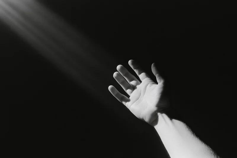 Hand reaching upward into a beam of light against a dark background