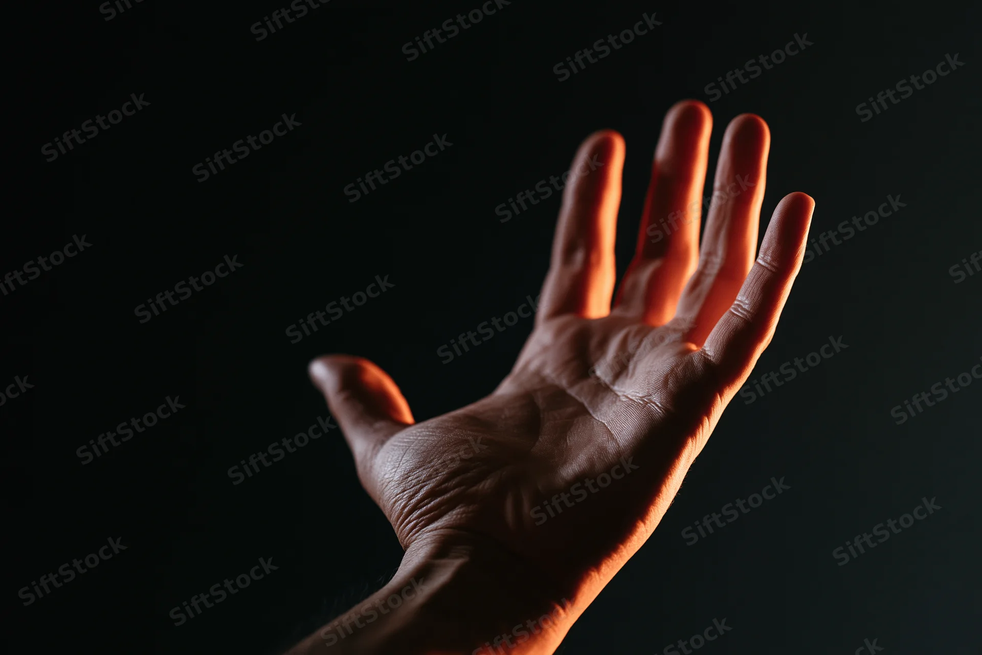 Hand with fingers splayed reaching upward against dark background