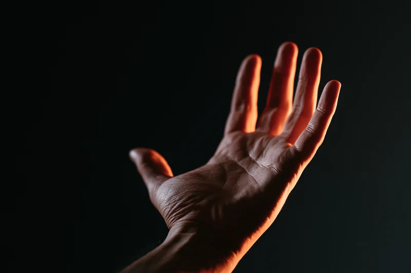 Hand with fingers splayed reaching upward against dark background