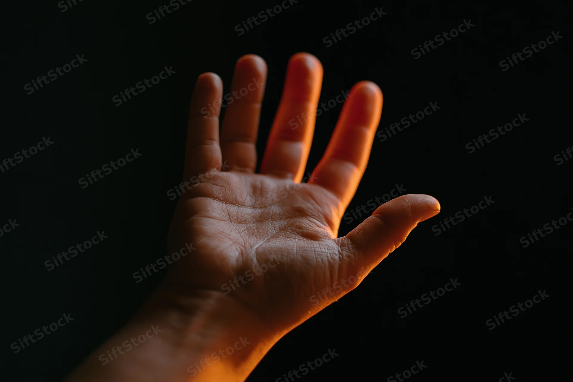 Hand with fingers splayed reaching upward against dark background