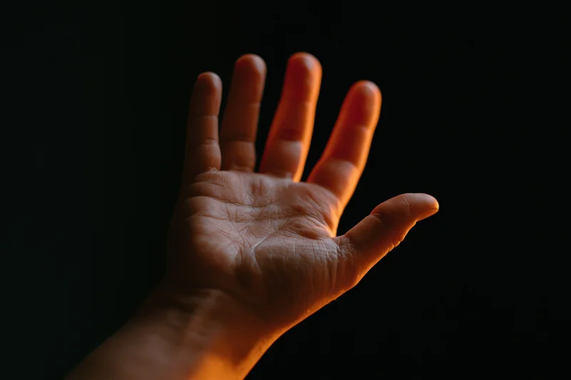 Hand with fingers splayed reaching upward against dark background
