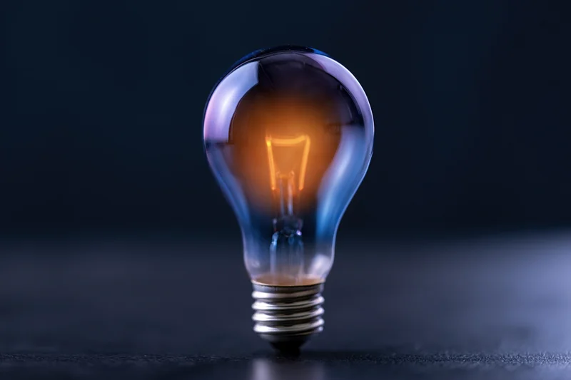 Glowing incandescent lightbulb standing upright on a dark surface