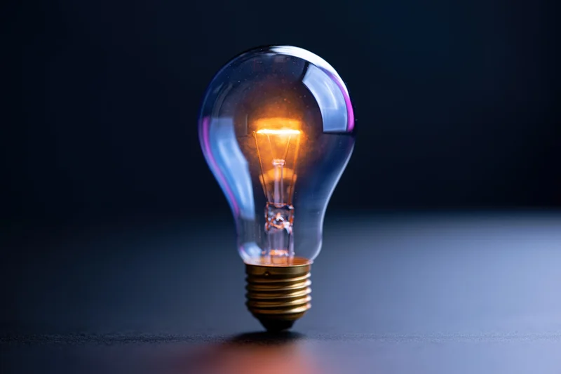 Glowing incandescent lightbulb standing upright on a dark surface