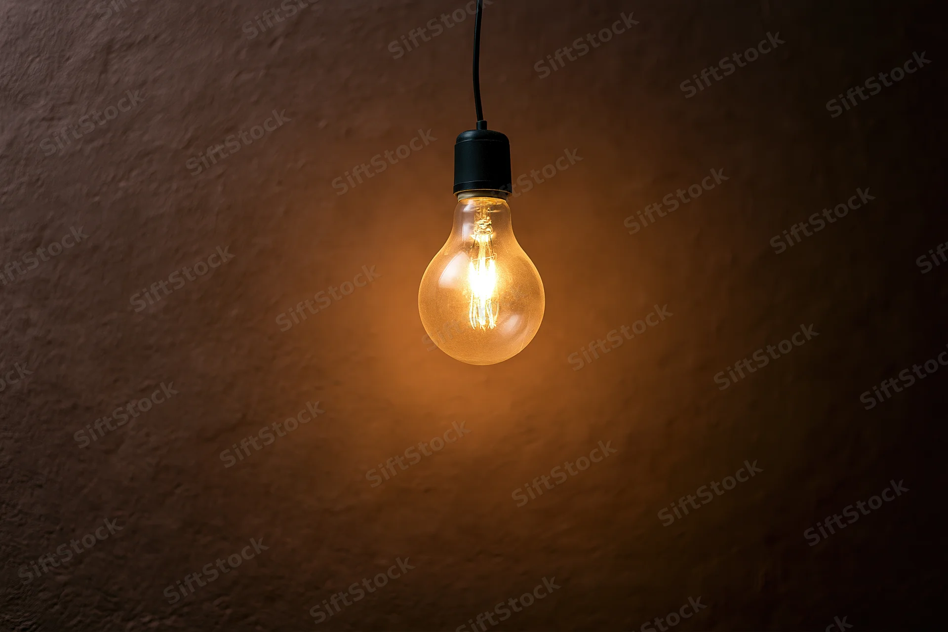 Single incandescent light bulb hanging and glowing against a dark textured wall