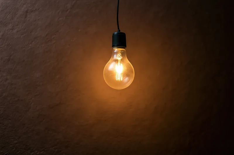 Single incandescent light bulb hanging and glowing against a dark textured wall