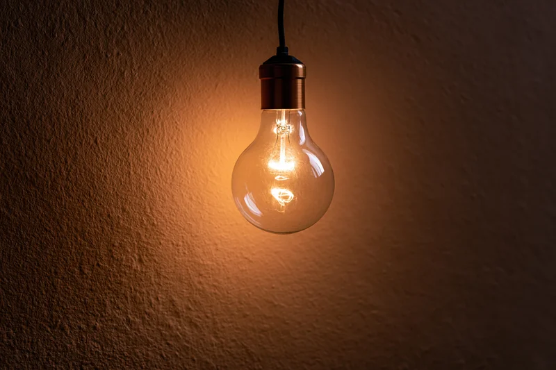 Single incandescent light bulb hanging and glowing against a textured dark wall