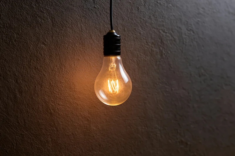 Single incandescent light bulb hanging and glowing against a dark textured wall