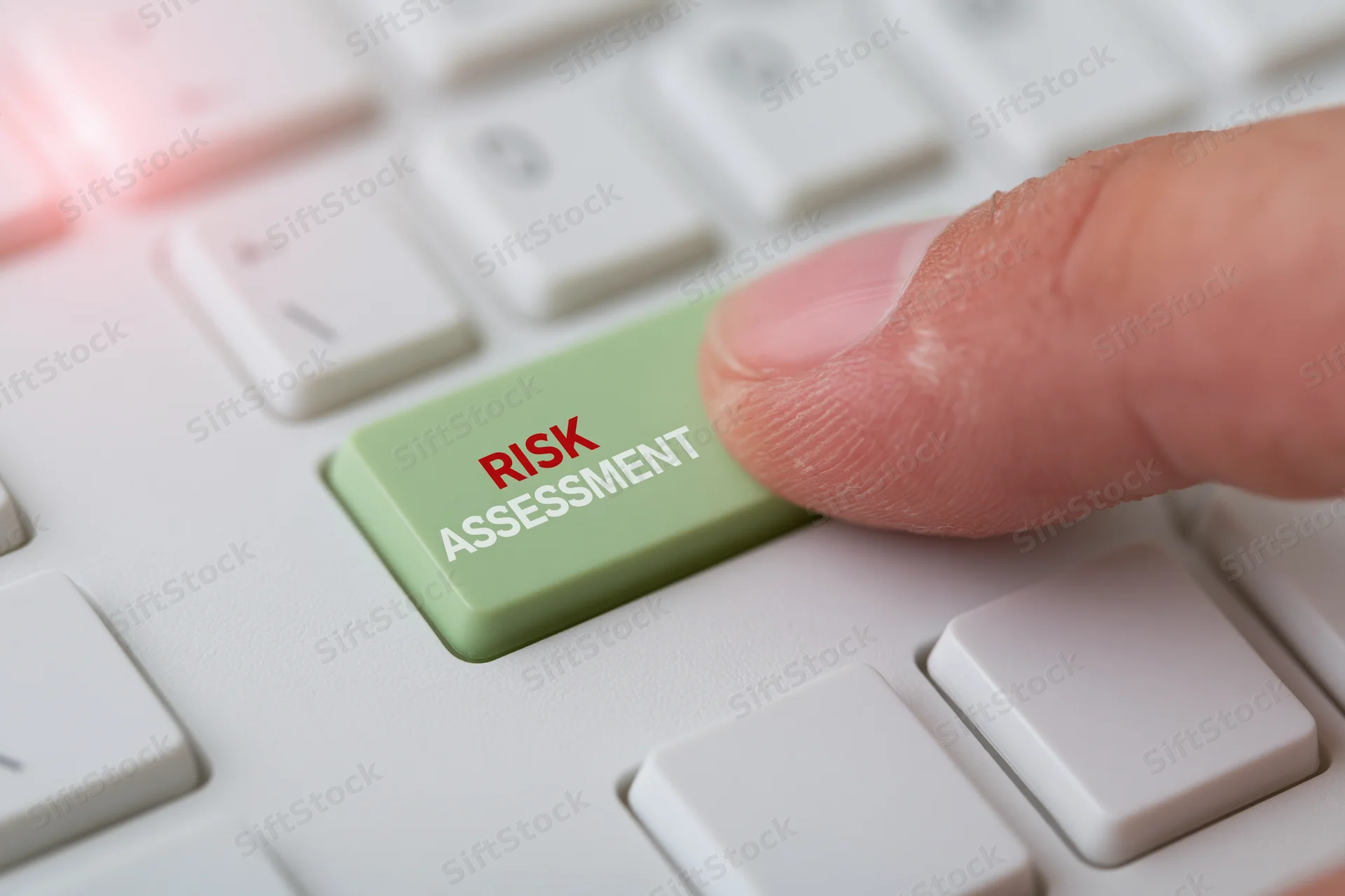 Finger pressing green keyboard key labeled risk assessment on white computer keyboard