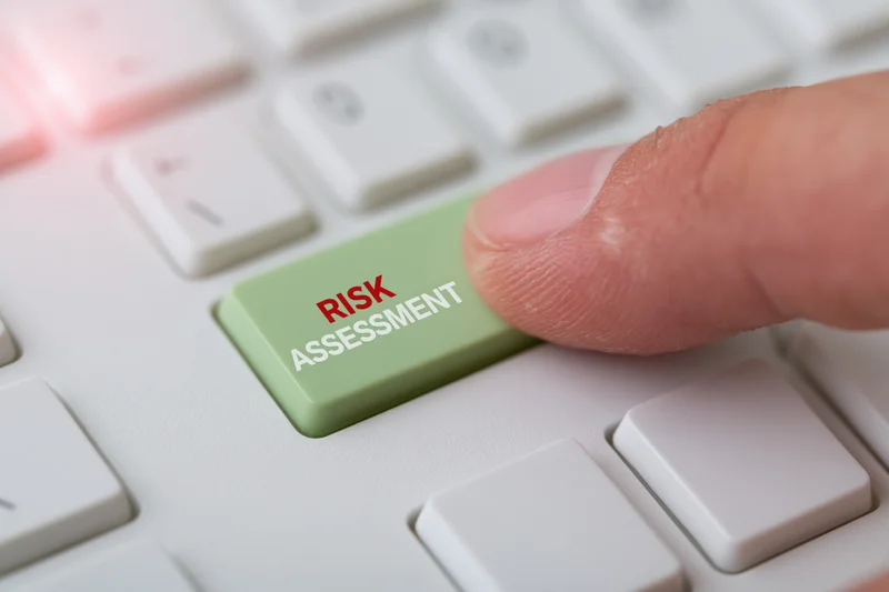 Finger pressing green keyboard key labeled risk assessment on white computer keyboard
