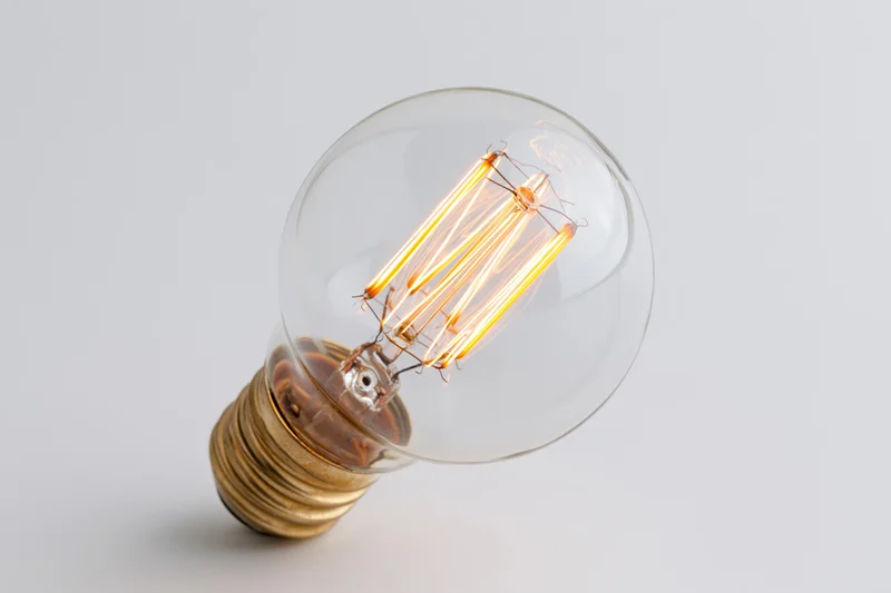 Lit edison incandescent light bulb with visible filament on white background