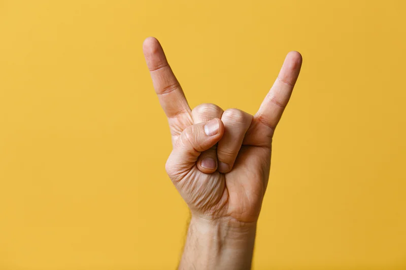 Male hand making rock-on devil horns gesture against yellow background