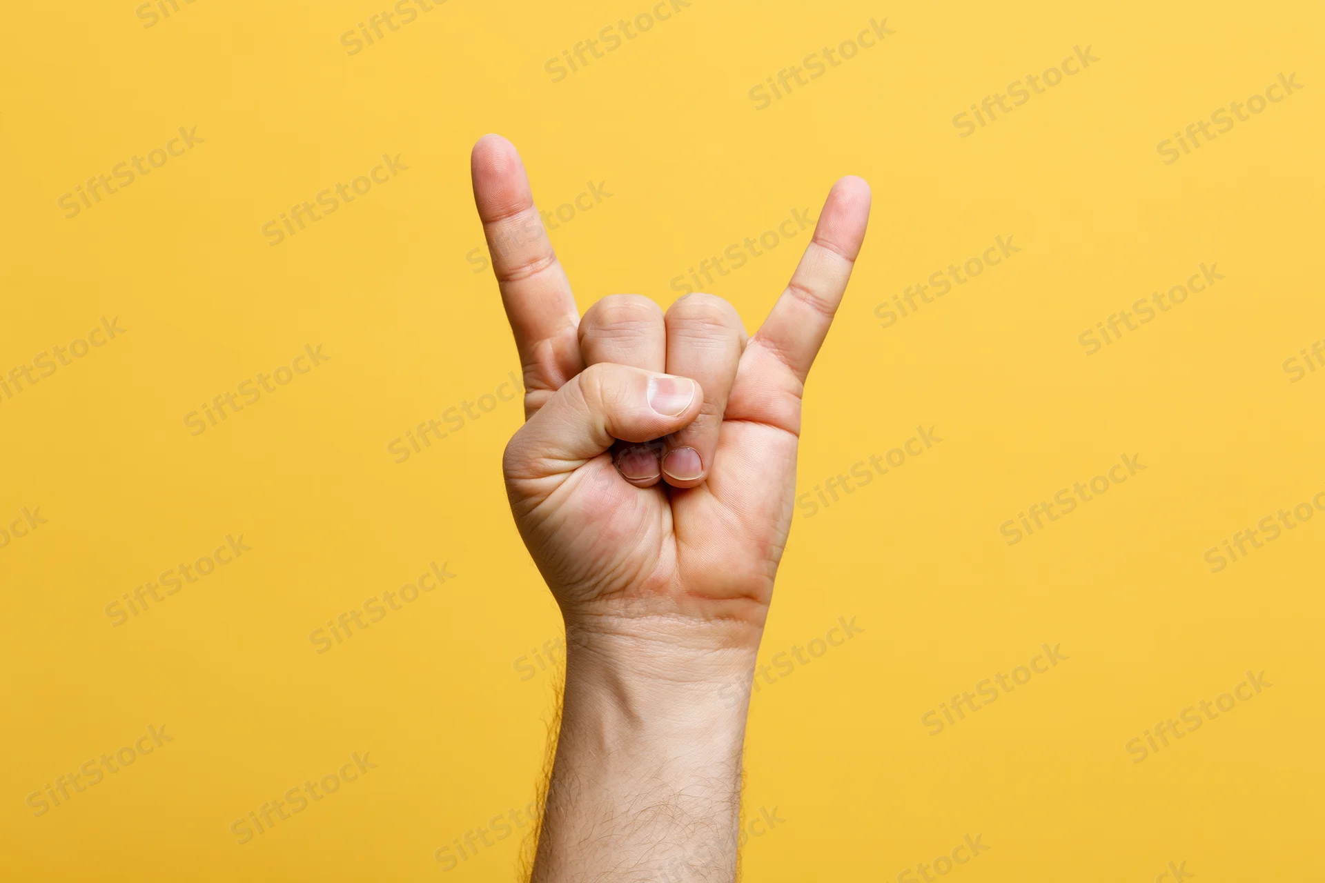 Male hand making rock-on devil horns gesture against yellow background