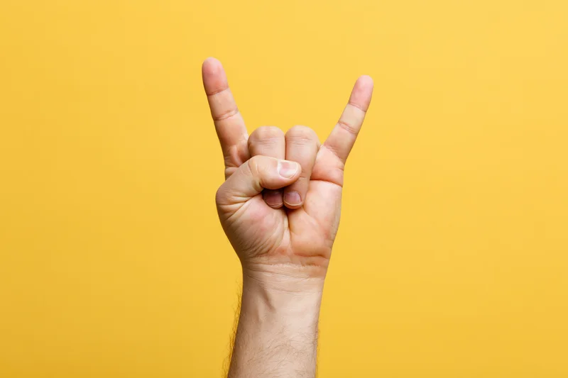 Male hand making rock-on devil horns gesture against yellow background