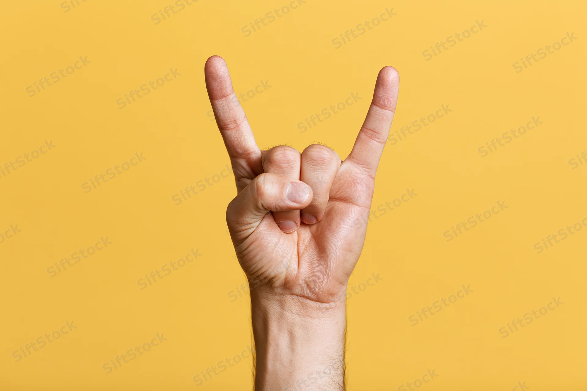 Male hand making rock-on devil horns gesture against yellow background