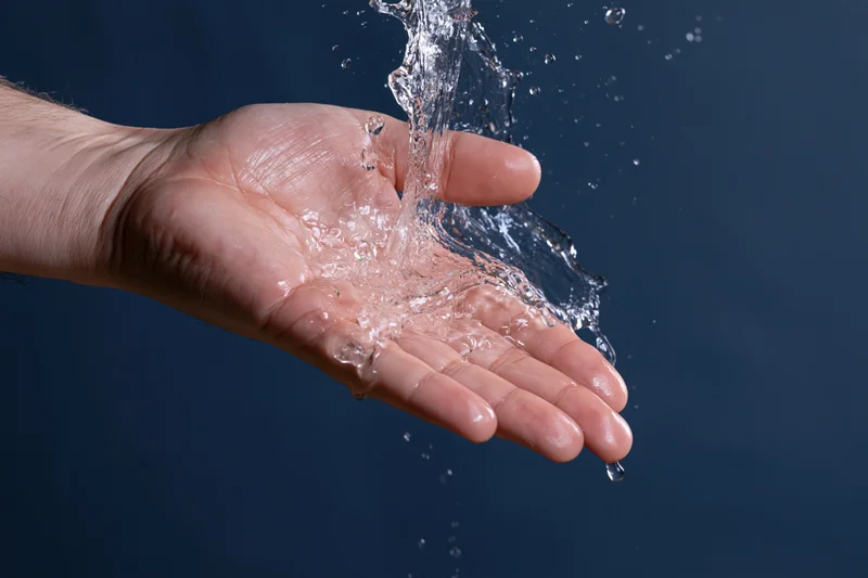 Open hand catching a dynamic water splash against a dark blue background