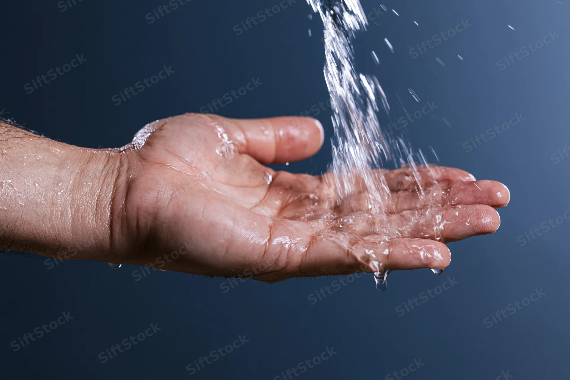 Open hand catching a stream of water against a dark blue background
