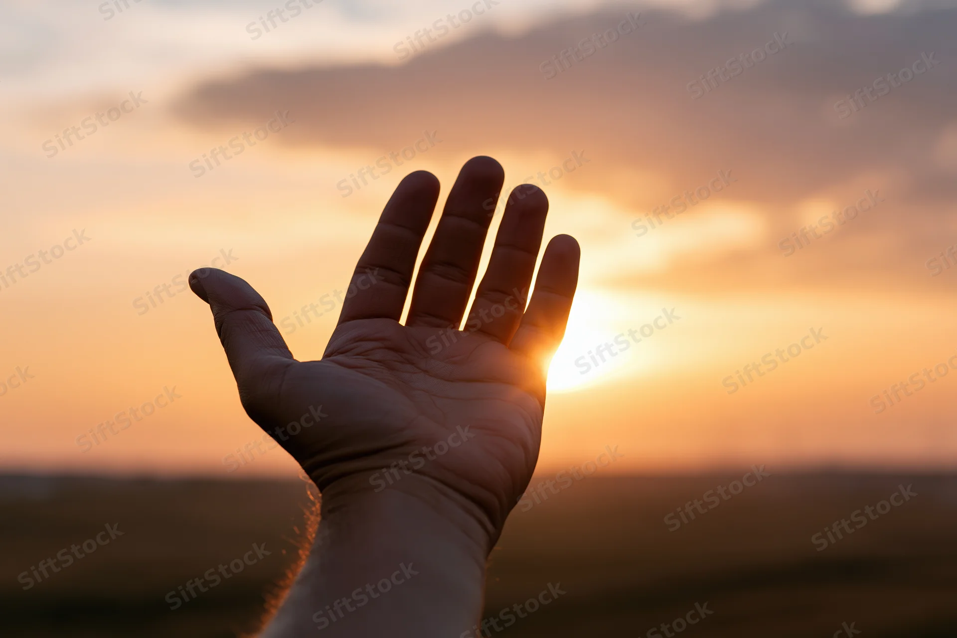 Open hand raised palm-up against a sunset sky