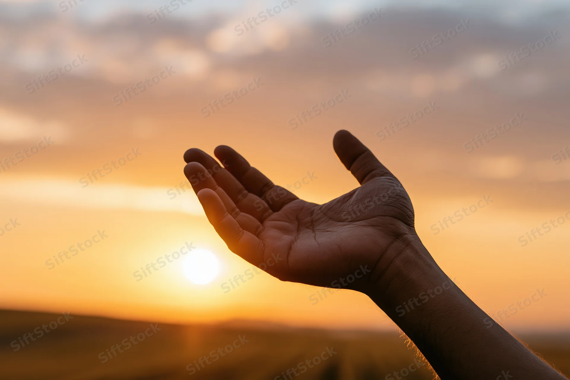 Open hand raised palm-up against a sunset sky