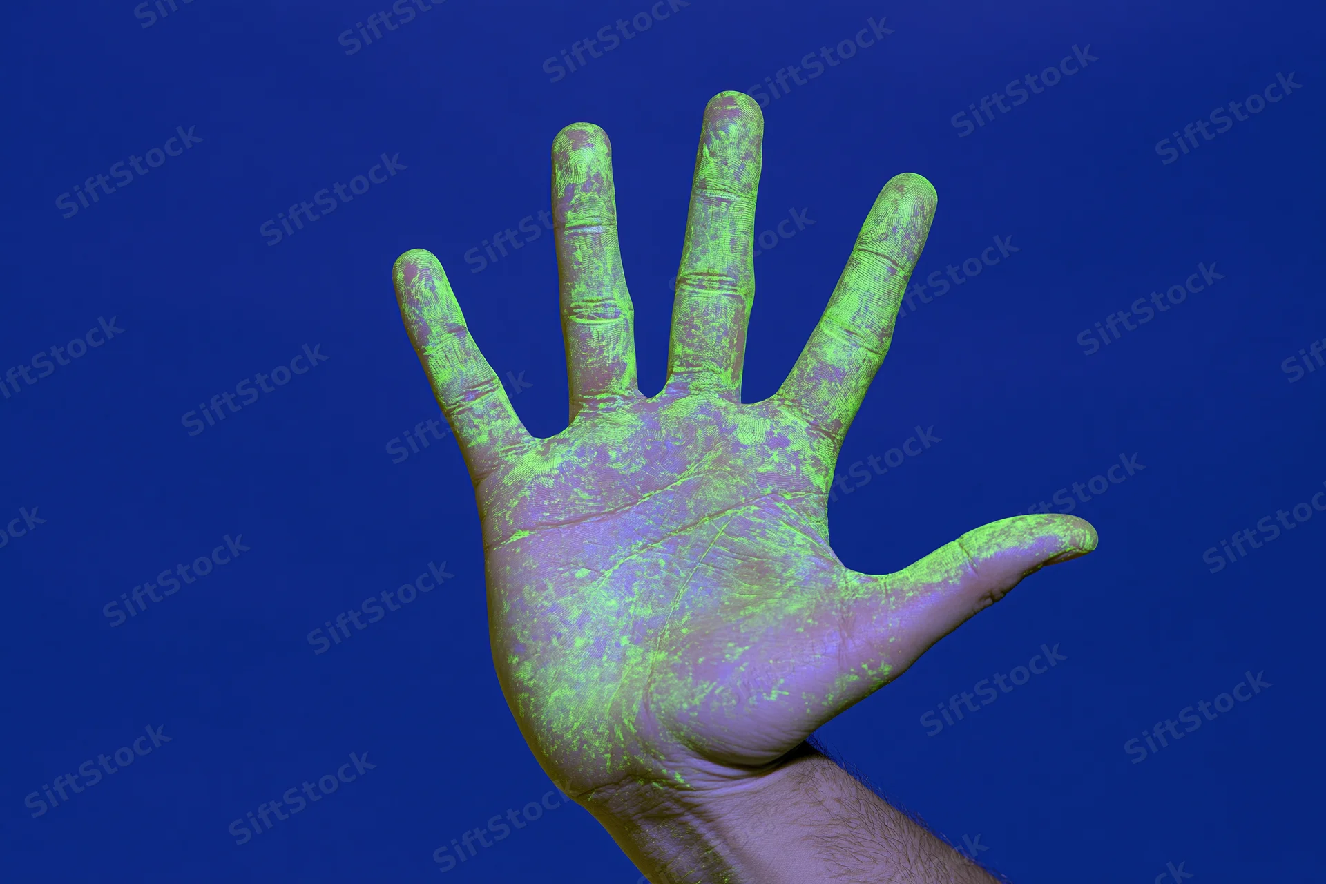 Open hand covered in glowing green paint raised against blue background