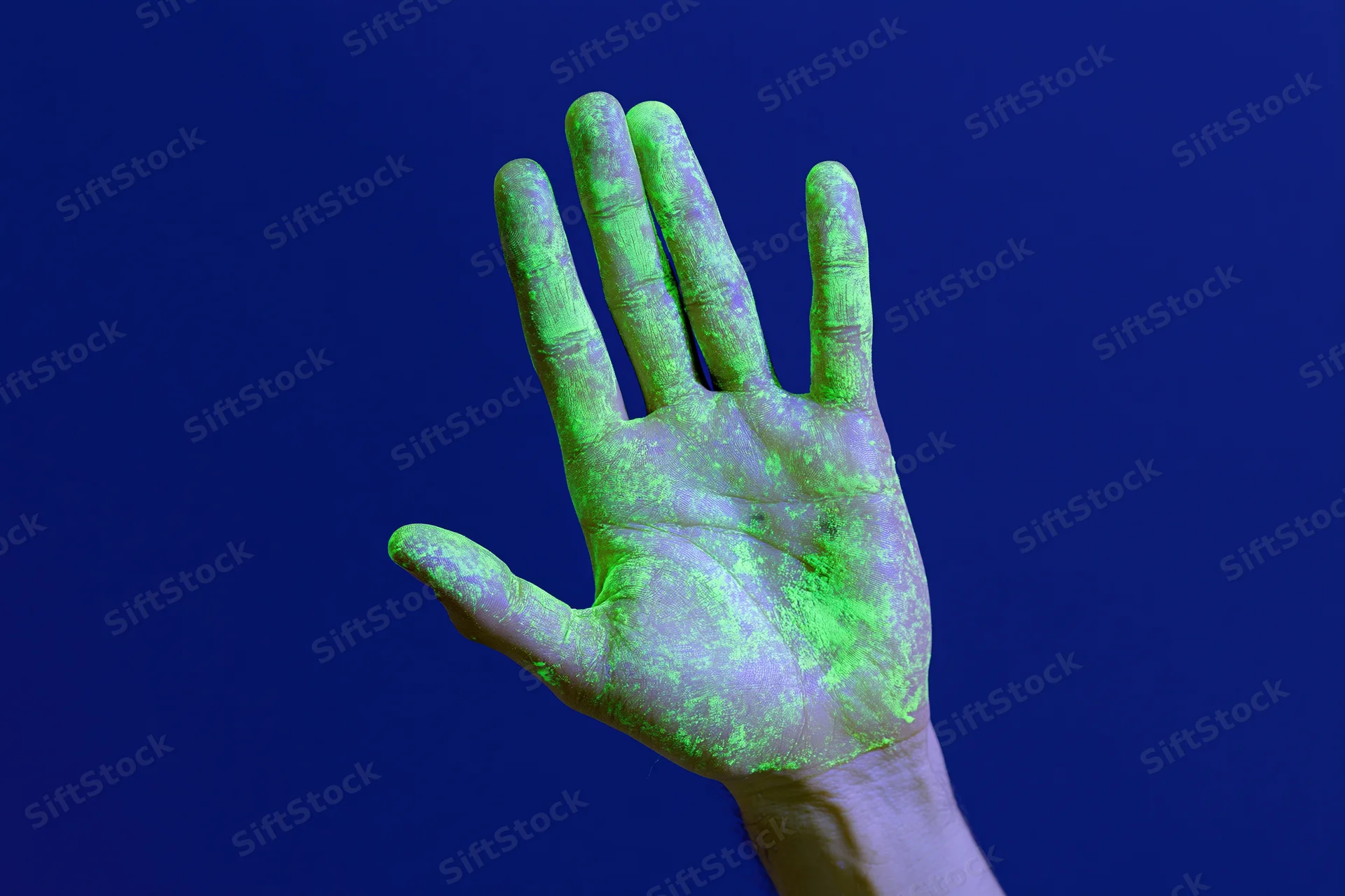 Open human hand covered in glowing green substance raised against dark blue background