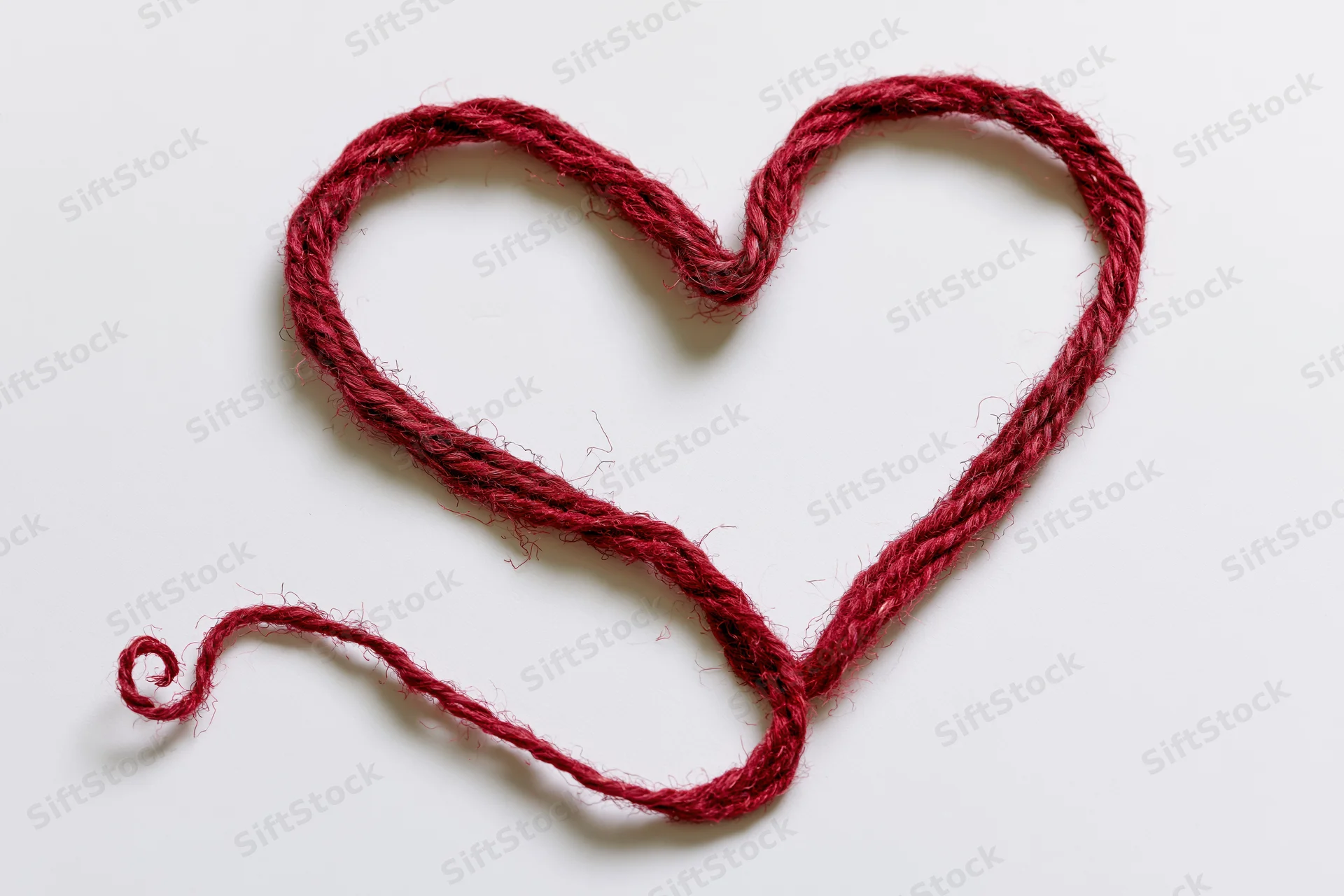 Red wool twine shaped into a heart on white background