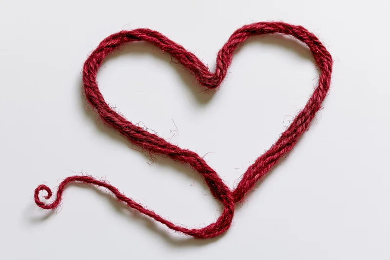 Red wool twine shaped into a heart on white background
