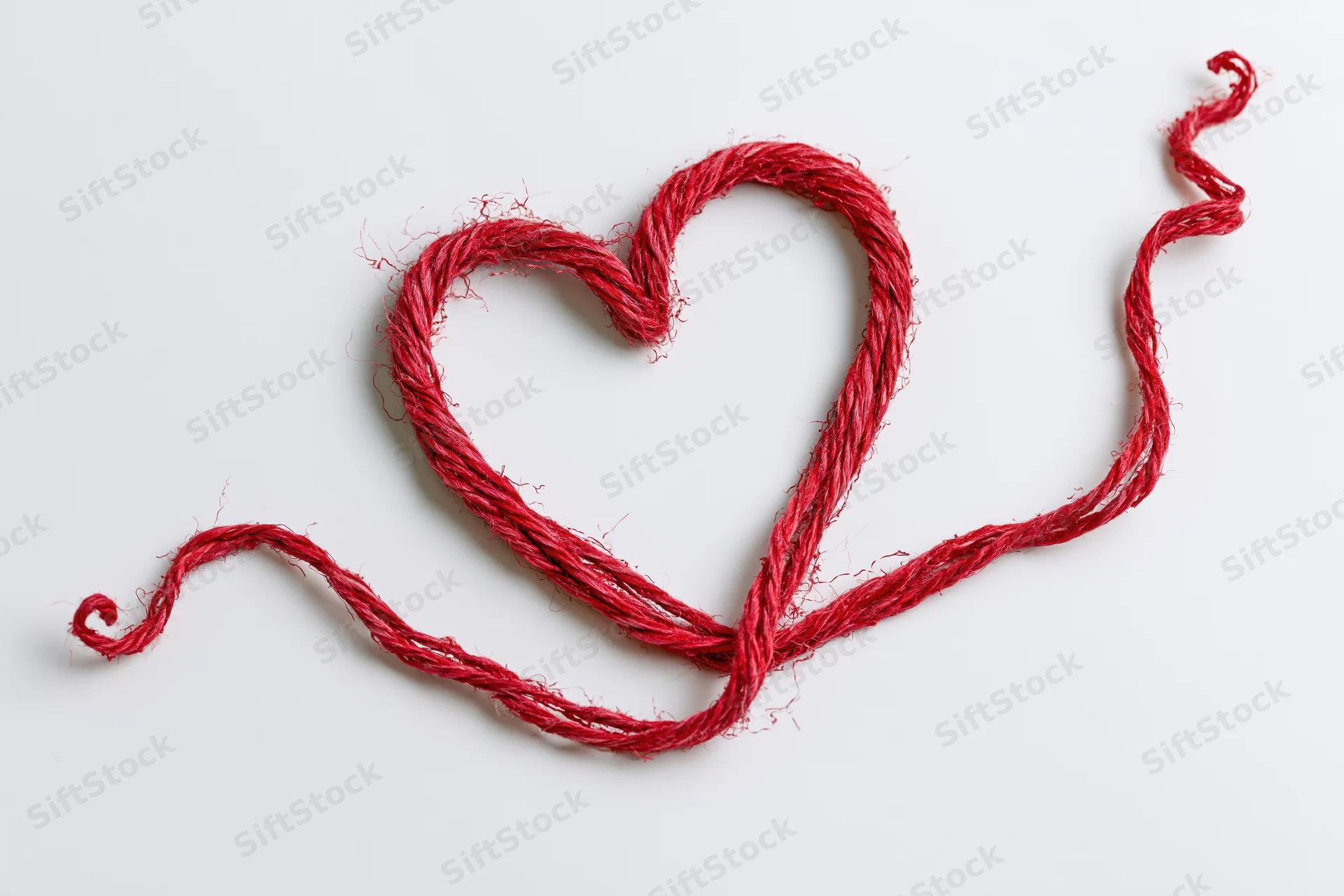 Red wool twine shaped into a heart on white background