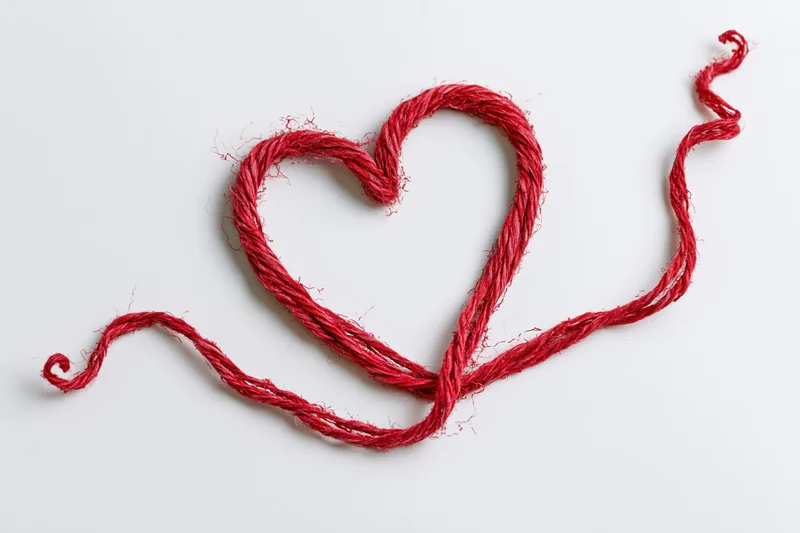 Red wool twine shaped into a heart on white background