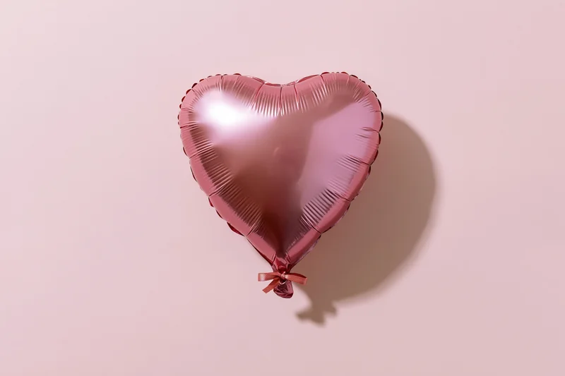 Pink foil heart-shaped balloon with ribbon on a soft pink surface