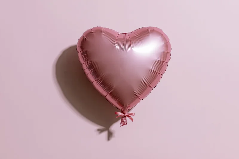 Pink foil heart-shaped balloon with ribbon floating against a soft pink background