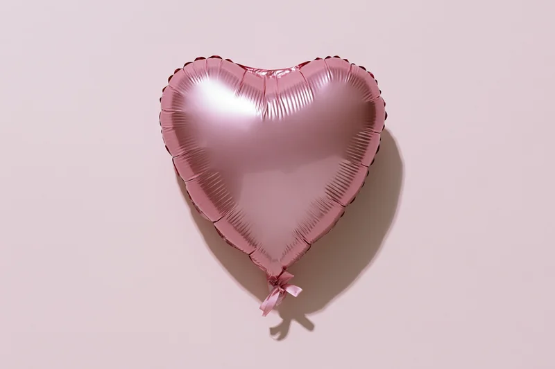 Pink foil heart-shaped balloon with ribbon on plain surface