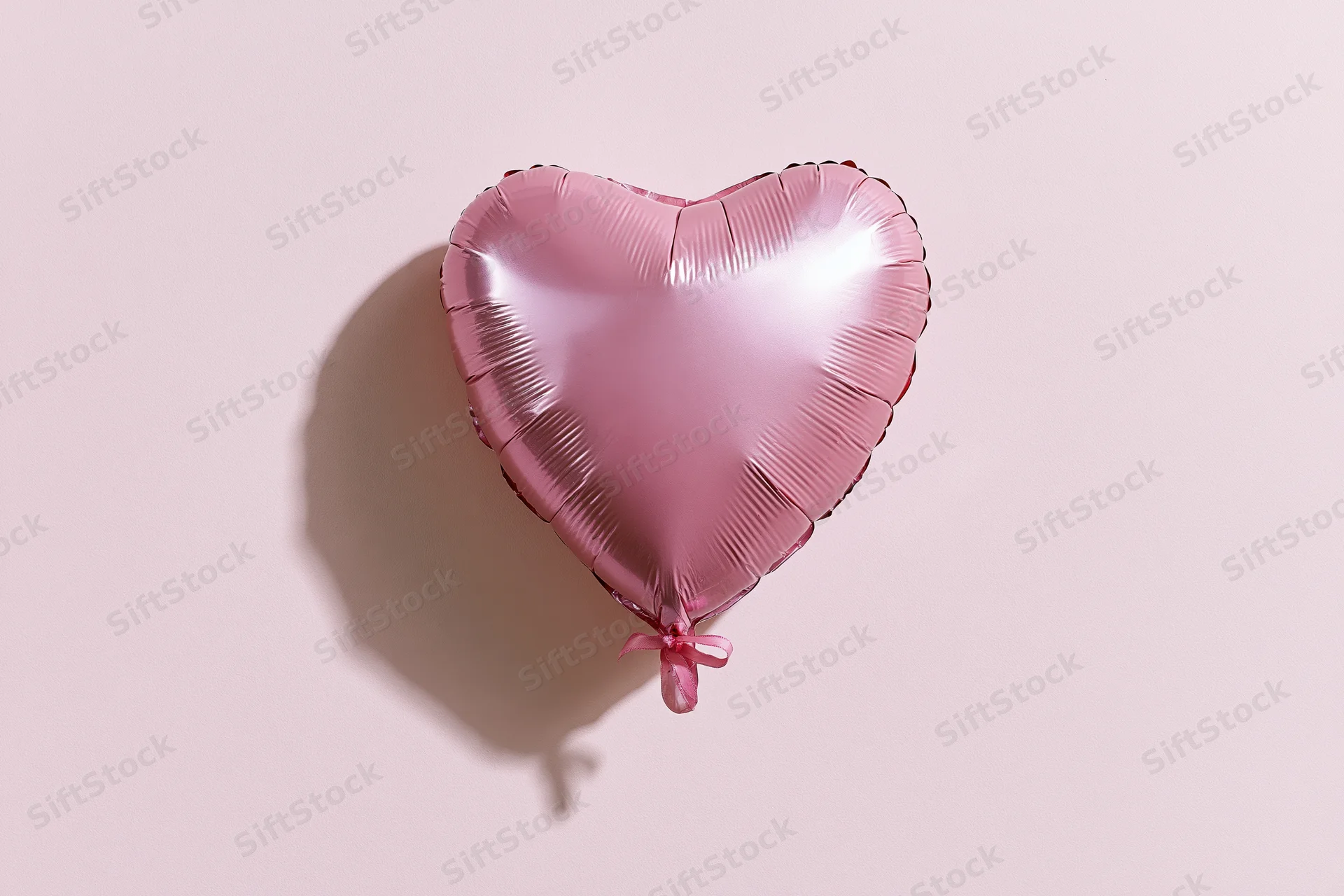 Pink foil heart-shaped balloon with ribbon against plain background