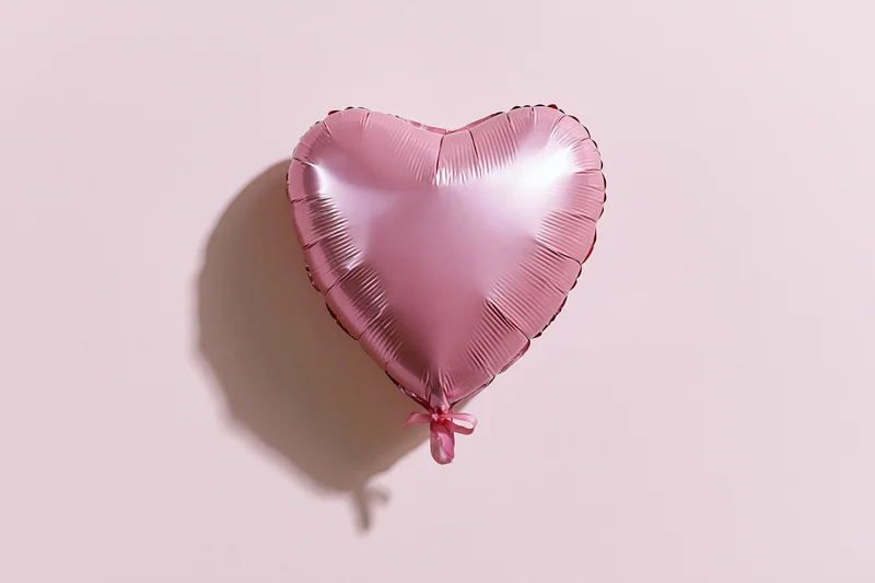 Pink foil heart-shaped balloon with ribbon against plain background